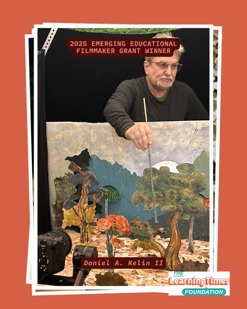 Behind-the-scenes photograph of Daniel A. Kelin II, a man with glasses and gray hair wearing a dark long-sleeved shirt, working with an elaborate multi-layered diorama set. The set features painted cutout layers depicting a natural landscape scene with stylized trees, foliage, flowers, and sky elements creating depth. Professional video cameras are visible in the foreground, positioned to film the miniature set. The scene is lit against a black background. The image is set on an orange background with white frame borders. Text at the top reads '2025 EMERGING EDUCATIONAL FILMMAKER GRANT WINNER' in orange, with 'Daniel A. Kelin II' labeled at the bottom. The Learning Times Foundation logo appears in the bottom right corner.